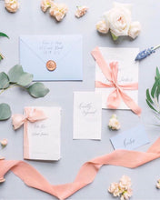 Load image into Gallery viewer, image of a pastel flat lay photo on a pale gray background with pink ribbon, calligraphy invitation suite, broze wax seal and flowers.