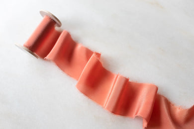 handmade and hand dyed coral pink silk ribbon. Hand frayed torn edge. On a wooden spool
